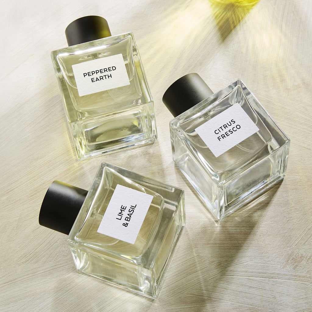 Three perfume bottles labeled 'Peppered Earth', 'Citrus Fresco', and 'Lime & Basil' on a light wooden surface.