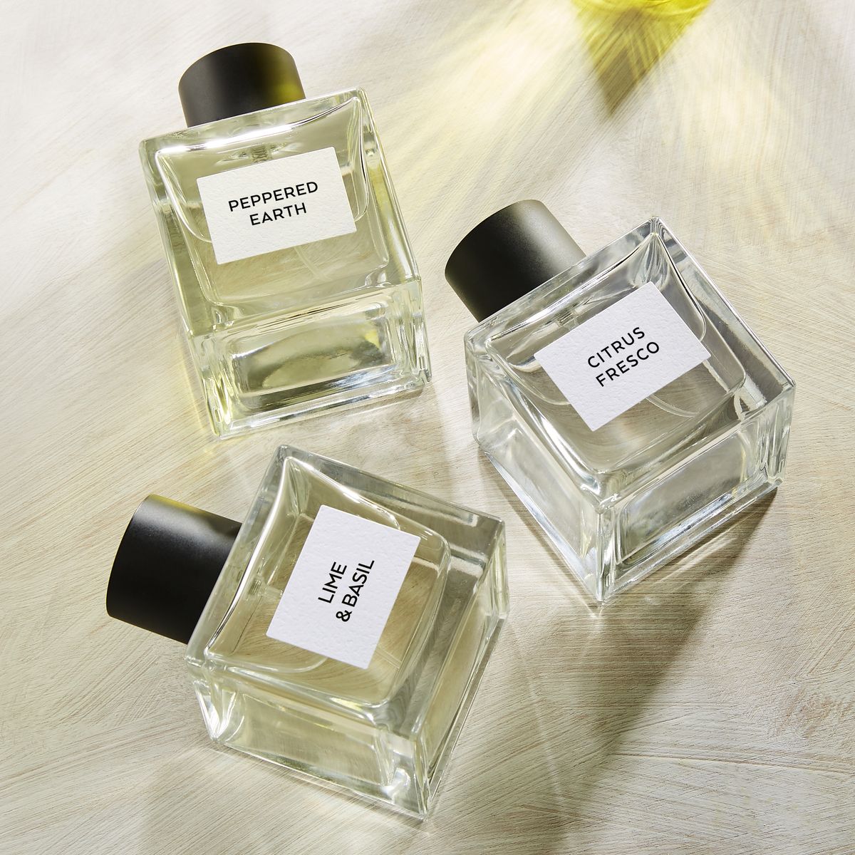 Three perfume bottles labeled 'Peppered Earth', 'Citrus Fresco', and 'Lime & Basil' on a light wooden surface.